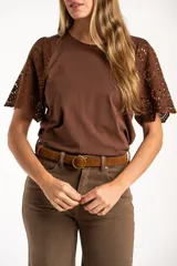 Remera de algodón peinado color negro, con mangas cortas de broderie con diseño calado y terminación festoneada. Presenta un corte oversize y cuello redondo.