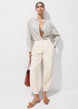 Pantalones vaqueros de tiro medio, estilo balloon con diseño crop y largo tobillero. Presentan detalle de pinzas, cierre de gancho y cremallera, dos bolsillos laterales y puños elásticos en los tobillos.