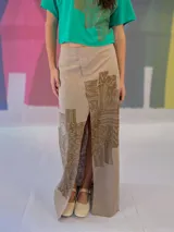 Falda larga blanca de lino y algodón con estampa exclusiva en cobre laminado. Corte asimétrico, tajo central y un bolsillo lateral. Cierre frontal con broches a presión.