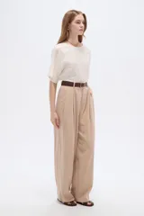 Pantalón de lyocell color beige, de tiro alto, corte ancho y diseño plisado con bolsillos laterales.