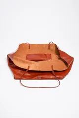 Bolso shopper de estructura blanda confeccionado en piel vacuna con acabado brillante. Cuenta con doble asa de hombro, costura central vertical y logo metálico de la marca en la base frontal.