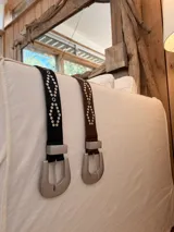 Cinturon de cuerina negra con tachas plateadas dispuestas en patron geometrico y hebilla metalica grande de estilo western.
