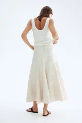 Pollera midi de tiro alto, corte circular con volumen y vuelo, confeccionada en tejido jacquard color blanco roto con textura. Posee forro interior y cierre oculto con corchete en la parte trasera.