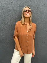 Camisa de seda color marrón chocolate, de corte holgado y manga corta con detalle de botón en el dobladillo. Presenta cuello clásico y cierre frontal con botones.