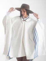 Poncho blanco de hilo de algodón grueso, con franjas azules en los laterales, flecos en el ruedo y el escudo nacional uruguayo bordado en la espalda.