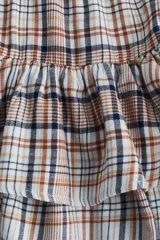 Pollera mini a cuadros en tonos tierra, azul marino y blanco. Diseño de tiro alto con elástico revestido en la cintura y cordón ajustable. Presenta dos volados horizontales que le dan volumen.