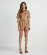 Camisa de manga corta confeccionada en cuero sintético color tostado, con cuello camisero, cierre frontal con botones en forma de corazón y dos bolsillos con solapa en el pecho.