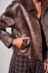 Campera de cuero vegano en tono marrón con acabado desgastado, corte recto y cierre frontal con botones a presión. Presenta cuello clásico y diseño minimalista.