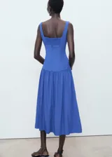 Vestido midi de color azul, sin mangas, con tirantes anchos y cuello escotado cuadrado. Presenta un diseño ajustado en el torso con corte evase y falda de corte midi con vuelo.
