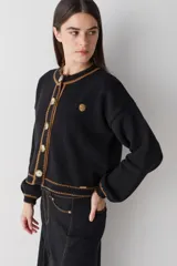 Cardigan de punto color marrón con detalles de ribete en color verde oliva en cuello, puños, ruedo y tapeta de botones. Presenta cierre frontal con botones grandes y un pequeño bordado en el pecho.