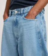 Pantalón de jean color celeste, modelo barrel, de tiro medio con trabillas para cinto, cierre frontal con botón y cremallera, bolsillos, recortes laterales y pinzas en las rodillas.