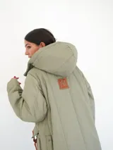 Abrigo largo color marrón con diseño acolchado de rombos, capucha y cierre frontal con botones a presión. Tiene bolsillos laterales y aberturas en los laterales inferiores.