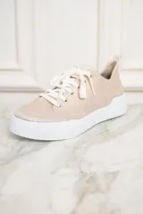 Zapatillas color arena metalizado con cordones blancos y suela blanca con estrías horizontales.