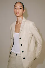 Blazer de Zara Woman Collection confeccionado en mezcla con lino, color beige con diseño de rayas finas verticales. Presenta cuello solapa, manga larga, bolsillos de parche en el delantero y cierre frontal con botones oscuros a contraste.