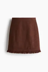 Pollera corta de tejido bouclé color marrón oscuro, de tiro alto y corte recto, con bajo desflecado.