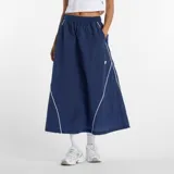 Pollera midi New Balance de tejido ripstop color azul marino, con cintura elástica, bolsillos laterales y detalles de líneas blancas en contraste. Presenta el logo de la marca en la parte inferior.
