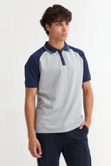Remera tipo polo de manga corta con diseño combinado, cuerpo en color gris y mangas y cuello en color azul marino. Presenta cierre frontal con botones y detalles de líneas finas en el cuello.