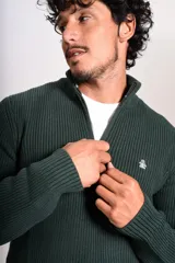 Sweater de punto acanalado en color verde oscuro, con cuello alto y cierre frontal parcial de un cuarto. Presenta puños y ruedo elásticos, con el logo de la marca bordado en el pecho.