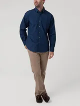 Camisa de hombre color azul marino, de manga larga con presillas para enrollar, cuello clásico, cierre de botones de madera y bolsillo en el pecho con logo bordado. Confeccionada en popelina 100% algodón orgánico.