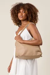 Cartera tipo hobo de ecocuero color beige, con textura granulada, cierre superior con cremallera, doble asa corta y correa larga regulable con cadena decorativa.