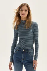 Polera de manga larga con cuello alto, confeccionada en tejido de algodón a rayas horizontales en tonos marrón y celeste. Presenta un calce ajustado al cuerpo y un pequeño bordado en el pecho.