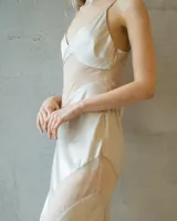 Vestido largo de satén color champagne, con escote en V profundo, tirantes finos y recortes geométricos laterales que estilizan la silueta.
