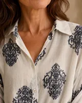 Camisa blanca de manga larga con estampado azul en contraste, cuello camisero y cierre frontal con botones.