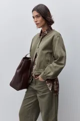 Campera de algodón verde militar, de calce relajado y largo corto, con cuello redondo, cierre frontal de botones metálicos, mangas largas y bolsillos delanteros funcionales.