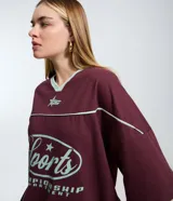 Remera de corte boxy color bordó, con cuello en V en color menta, mangas cortas con recortes y estampa frontal con temática deportiva en color menta.