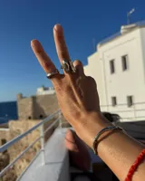 Anillo de diseño orgánico y macizo con forma irregular, elaborado en metal con acabado brillante. Presenta una estructura abierta que permite su ajuste.