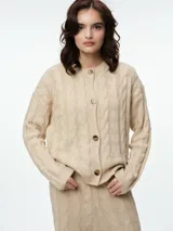 Cárdigan de punto con diseño de ochos, color beige, con cuello redondo, cierre frontal de botones tipo carey y puños acanalados.