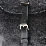 Mochila de cuero negro con textura granulada, diseño de solapa con cierre de hebilla metálica ajustable y logo de la marca grabado en el frente.