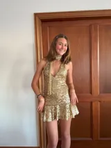 Vestido corto negro con estampado de plumas doradas, escote en V, breteles finos cruzados en la espalda, cut-outs laterales y volado en el ruedo.