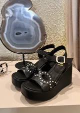 Sandalias de plataforma corrida color marrón, con tiras en el empeine decoradas con perforaciones y tachas metálicas, y tira ajustable con hebilla en el tobillo.