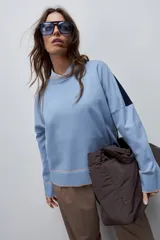 Sweater tejido celeste de calce relajado con cuello redondo, hombros caídos y puños y ruedo acanalados con detalles en tono tostado.
