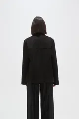 Chaqueta de gamuza sintética en color negro, con cuello solapa, cierre frontal con botones y bolsillos delanteros. Presenta un corte holgado y mangas largas.