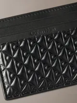 Tarjetero Calvin Klein de cuero negro con diseño compacto y múltiples ranuras para tarjetas. Presenta un sofisticado patrón geométrico grabado en relieve en la parte inferior y el logo de la marca grabado en la parte superior.