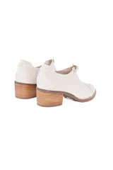 Zapato cerrado tipo mocasín con taco cuadrado de madera, confeccionado en cuero con textura de reptil en color crema. Presenta un detalle de hebilla metálica dorada en el empeine.