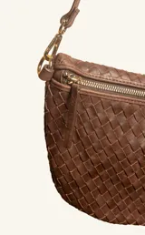 Bandolera de gamuza color marrón con diseño de media luna, decorada con tachas metálicas doradas distribuidas en el frente. Cuenta con cierre superior metálico y correa larga ajustable para llevar cruzada.