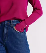 Suéter de punto color rosado, con cuello barco, mangas largas y puños con botones decorativos. El dobladillo también es acanalado.