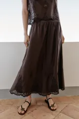 Falda midi marrón oscuro, con diseño fluido y voluminoso, tiro alto y detalles de bordados a tono en el ruedo.