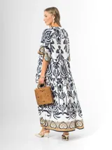Maxi vestido blanco con estampado paisley en azul marino y detalles en tonos dorados, con cuello en V, mangas amplias y diseño escalonado.