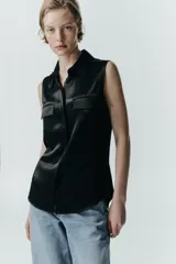 Camisa sin mangas de tejido satinado, con cuello solapa, cierre frontal con botones ocultos y bolsillos de plastrón con solapa en el delantero. Presenta un bajo asimétrico y corte recto.