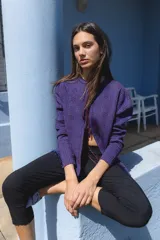 Cardigan de punto en color violeta con destellos de lurex, diseño de manga larga y cierre frontal con lazos. Presenta detalles de mostacillas en el ruedo.