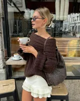 Buzo tejido de punto en color marrón chocolate, con diseño off-shoulder, cuello amplio y mangas largas con puños acanalados. Presenta una textura acanalada y un calce relajado.