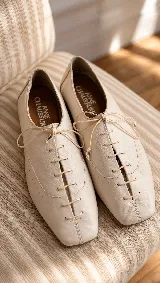 Zapato acordonado tipo oxford de cuero color off-white, con punta cuadrada, costuras decorativas y cordones finos al tono.