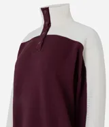 Buzo deportivo de corte oversized, con diseño bicolor en bordó y blanco. Presenta cuello alto con cierre de botones a presión, mangas largas con textura acanalada y puños elásticos.
