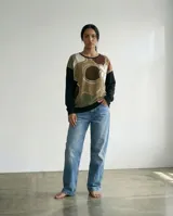 Remera tipo poncho de silueta amplia y relajada, confeccionada en una combinación de jersey y viscosa. Presenta un diseño bicolor con un panel frontal estampado con formas orgánicas en tonos tierra y verde, y mangas y espalda en color negro.