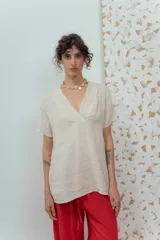 Blusa de lino color beige de calce relajado, con escote en V y detalles de pliegues frontales. Posee mangas cortas y una silueta suelta.