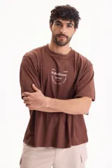 Remera oversize de manga corta en color marrón, confeccionada en 100% algodón. Presenta un diseño gráfico estampado en la espalda con inscripciones en color blanco.